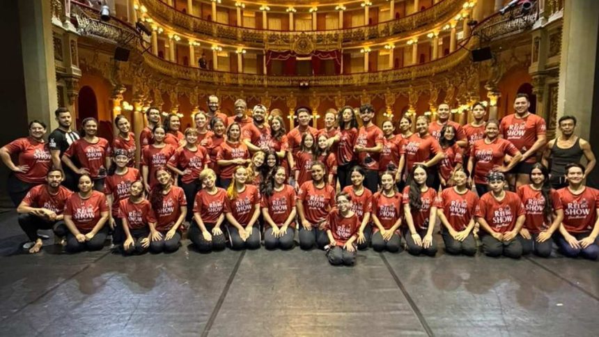 Grupo de artistas do 'Rei do Show' posando no Teatro Amazonas, com figurino vermelho.