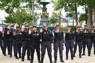 Grupo de policiais femininas em uniforme posando em frente a um chafariz, com mãos levantadas.