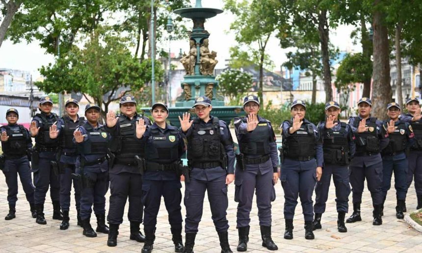 Grupo de policiais femininas em uniforme posando em frente a um chafariz, com mãos levantadas.
