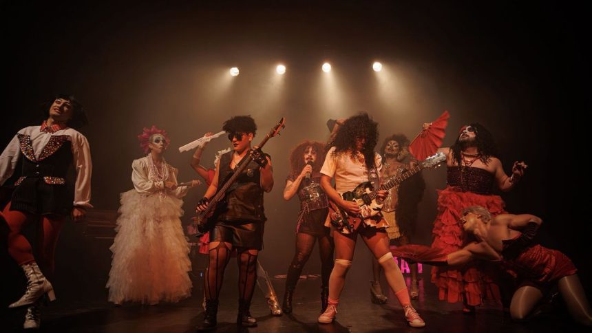 Grupo de teatro performando em palco escuro, com figurinos extravagantes e luzes