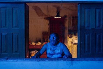 Homem assustado em janela com tela, cena do filme 'Mata-Gato'.