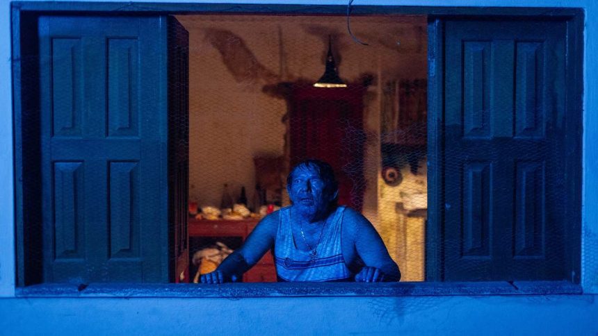 Homem assustado em janela com tela, cena do filme 'Mata-Gato'.