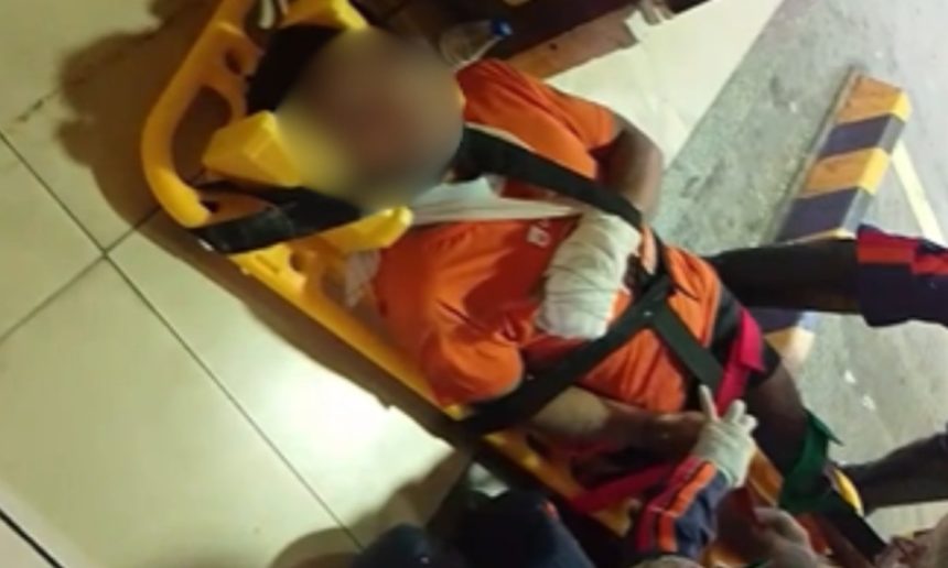 Homem ferido em maca com curativo no braço, possivelmente vítima de agressão.