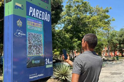 Homem usando smartphone para escanear código QR em painel de informações 'Paredão' em Manaus, Amazonas.