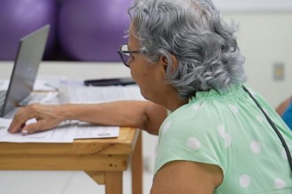 Idosa em atendimento na Defensoria Pública, utilizando computador.