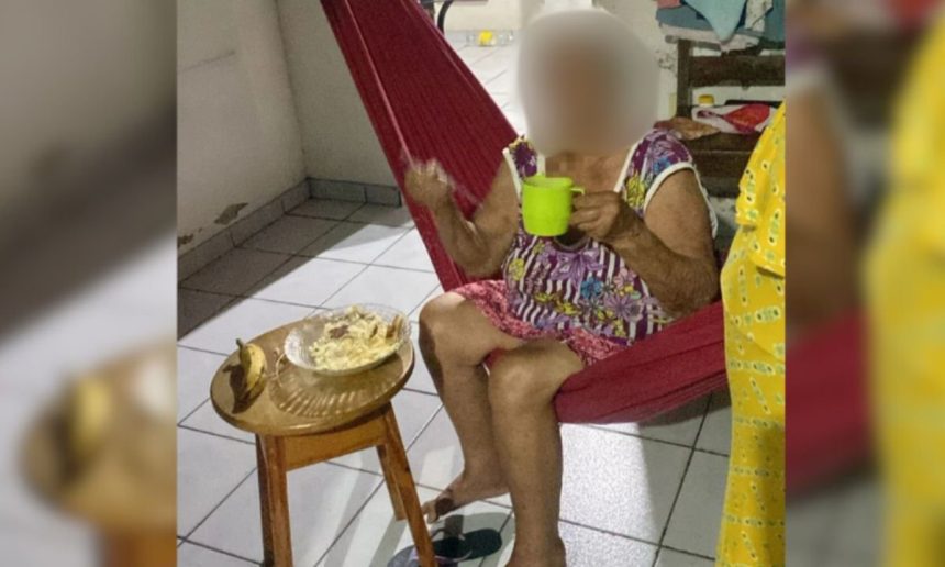 Idosa em rede comendo, simbolizando a situação de fome e abandono. Há comida em uma mesa próxima.