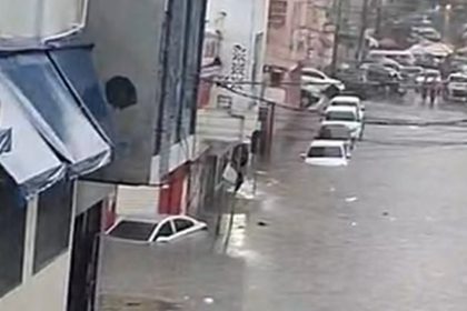 Imagem de rua alagada com carros submersos e lojas no centro de Manaus.