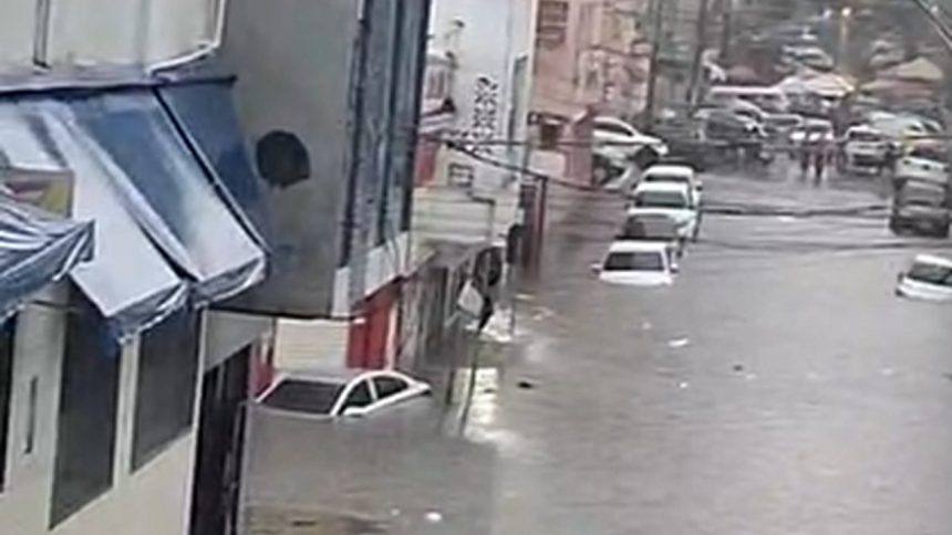 Imagem de rua alagada com carros submersos e lojas no centro de Manaus.