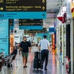 Interior de aeroporto com sinalização e pessoas andando.