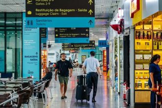 Interior de aeroporto com sinalização e pessoas andando.