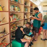 Interior de biblioteca móvel do Sesc, com pessoas lendo livros.