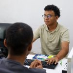 Jovens em ambiente de trabalho, focados em seus computadores, possivelmente em busca de emprego.