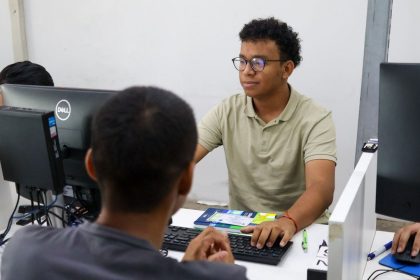 Jovens em ambiente de trabalho, focados em seus computadores, possivelmente em busca de emprego.