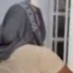 Mulher com boné cinza, vista de costas, em um ambiente interno.