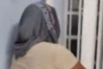 Mulher com boné cinza, vista de costas, em um ambiente interno.