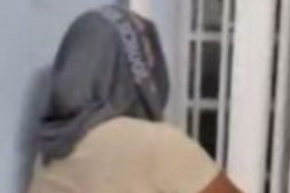 Mulher com boné cinza, vista de costas, em um ambiente interno.