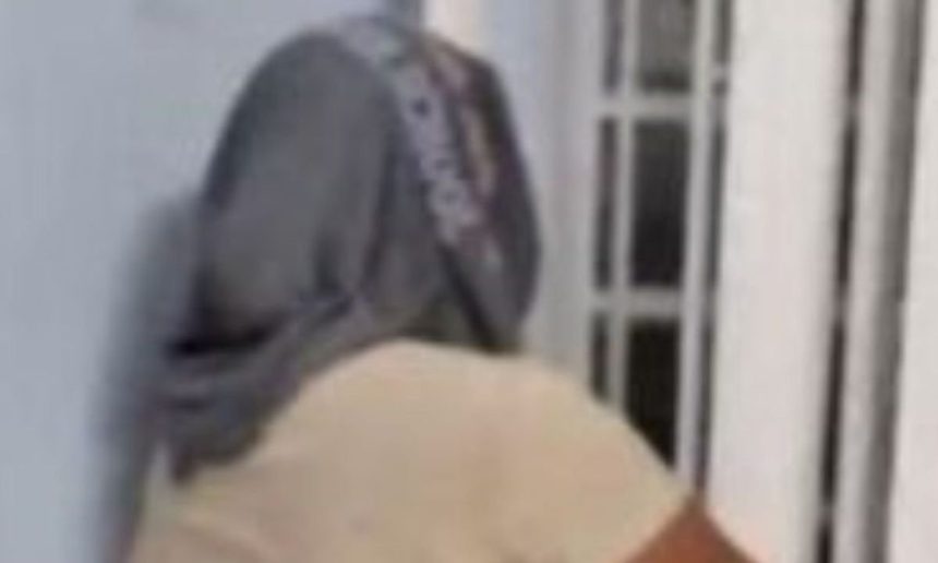 Mulher com boné cinza, vista de costas, em um ambiente interno.