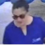 Mulher com óculos escuros vestindo camisa azul, possível suspeita em caso de ameaça.