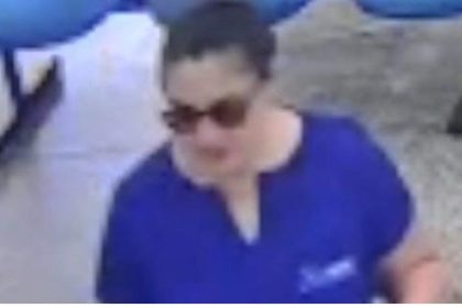 Mulher com óculos escuros vestindo camisa azul, possível suspeita em caso de ameaça.