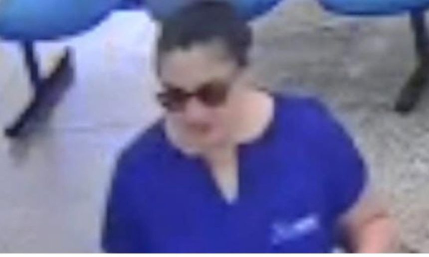 Mulher com óculos escuros vestindo camisa azul, possível suspeita em caso de ameaça.