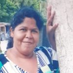 Mulher desaparecida em Manaus, segurando árvore, com expressão sorridente