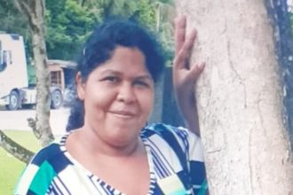 Mulher desaparecida em Manaus, segurando árvore, com expressão sorridente