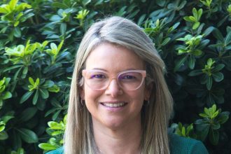 Mulher sorrindo com óculos em frente a folhagens, possivelmente representando o Sicredi