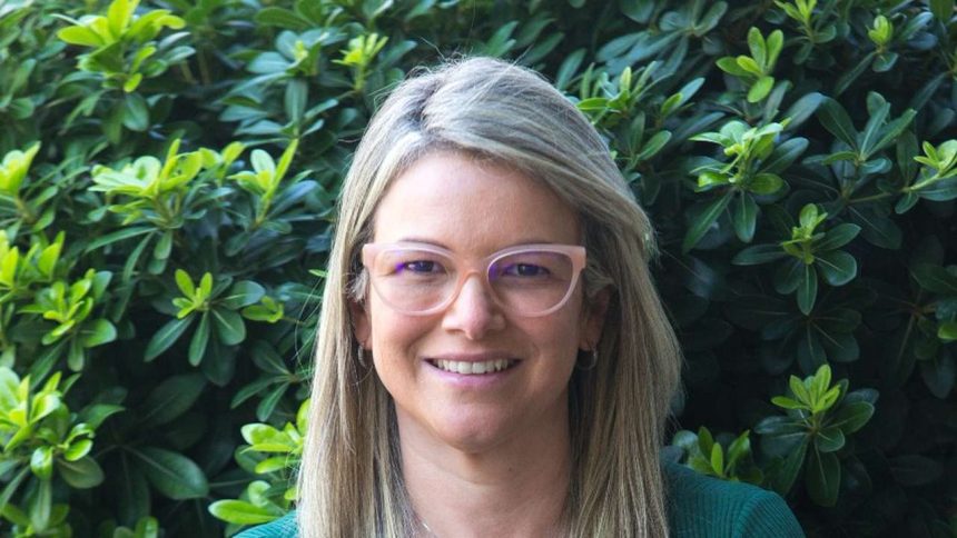 Mulher sorrindo com óculos em frente a folhagens, possivelmente representando o Sicredi