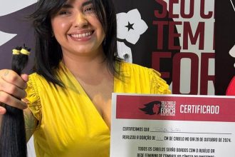 Mulher sorrindo segura mecha de cabelo doada para campanha Outubro Rosa.