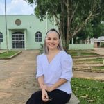 Mulher sorrindo sentada em banco de pedra em frente à igreja.