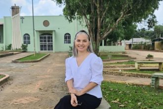 Mulher sorrindo sentada em banco de pedra em frente à igreja.
