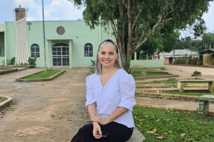 Mulher sorrindo sentada em banco de pedra em frente à igreja.