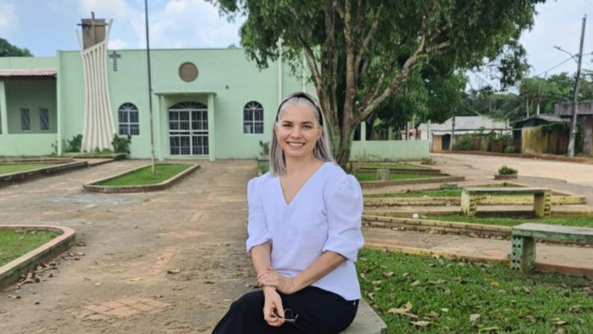 Mulher sorrindo sentada em banco de pedra em frente à igreja.