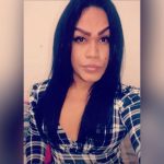 Mulher trans com cabelo preto e camisa xadrez, foto de perfil.