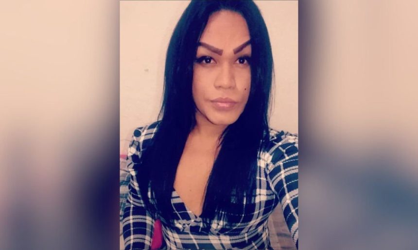 Mulher trans com cabelo preto e camisa xadrez, foto de perfil.