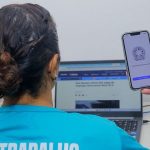 Mulher utilizando computador com celular mostrando Carteira de Trabalho Digital, Sine Manaus.