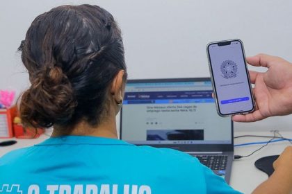 Mulher utilizando computador com celular mostrando Carteira de Trabalho Digital, Sine Manaus.