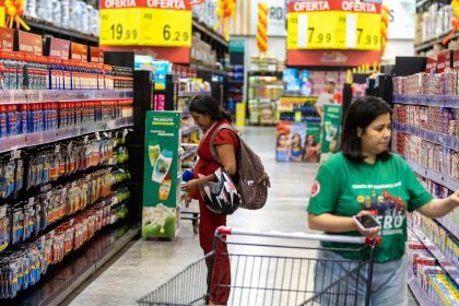 Mulheres comprando em supermercado, com promoções de produtos. Uma delas está grávida e a outra com carrinho de compras.