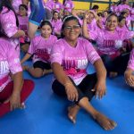 Mulheres em aula de defesa pessoal vestindo camisetas rosas e faixas