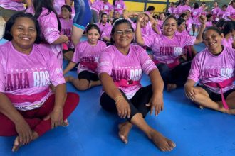 Mulheres em aula de defesa pessoal vestindo camisetas rosas e faixas