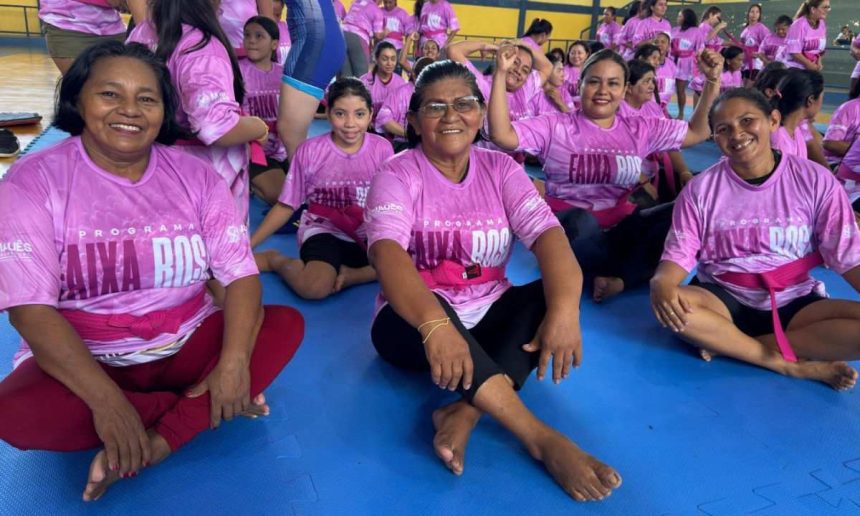 Mulheres em aula de defesa pessoal vestindo camisetas rosas e faixas