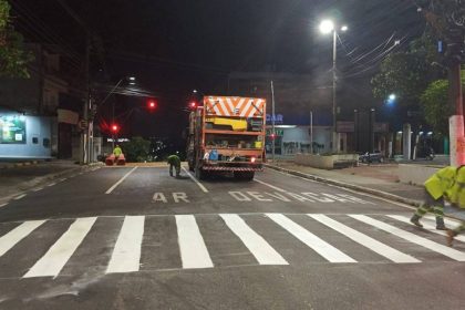 Operários trabalhando na sinalização de trânsito em rua à noite, com caminhão e faixas de pedestres
