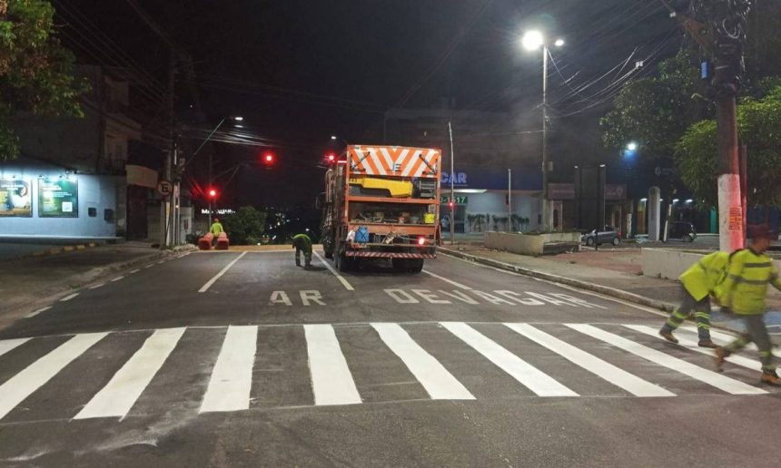 Operários trabalhando na sinalização de trânsito em rua à noite, com caminhão e faixas de pedestres