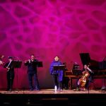 Orquestra Barroca do AM em concerto, com músicos tocando instrumentos de corda e sopro no palco.