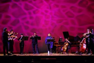 Orquestra Barroca do AM em concerto, com músicos tocando instrumentos de corda e sopro no palco.