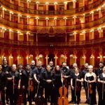 Orquestra de Câmara em concerto, com músicos em palco de teatro histórico.