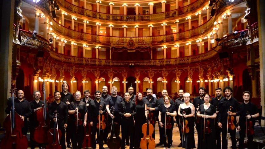 Orquestra de Câmara em concerto, com músicos em palco de teatro histórico.