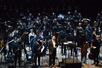 Orquestra no palco do Teatro Amazonas, com maestro em destaque. Apresentação musical 'Assim falou Zaratustra'.