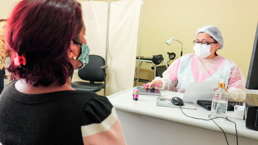 Paciente em consulta médica com profissional de saúde usando máscara e equipamentos de proteção individual.