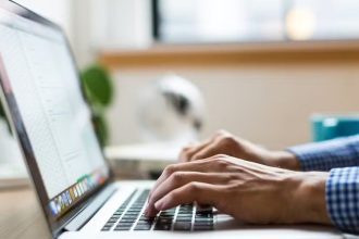 Pessoa digitando em um laptop, com foco nas mãos e teclado